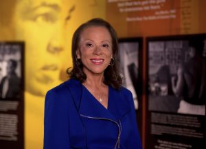 Lonnie Ali smiling in a suit with Muhammad Ali museum in background